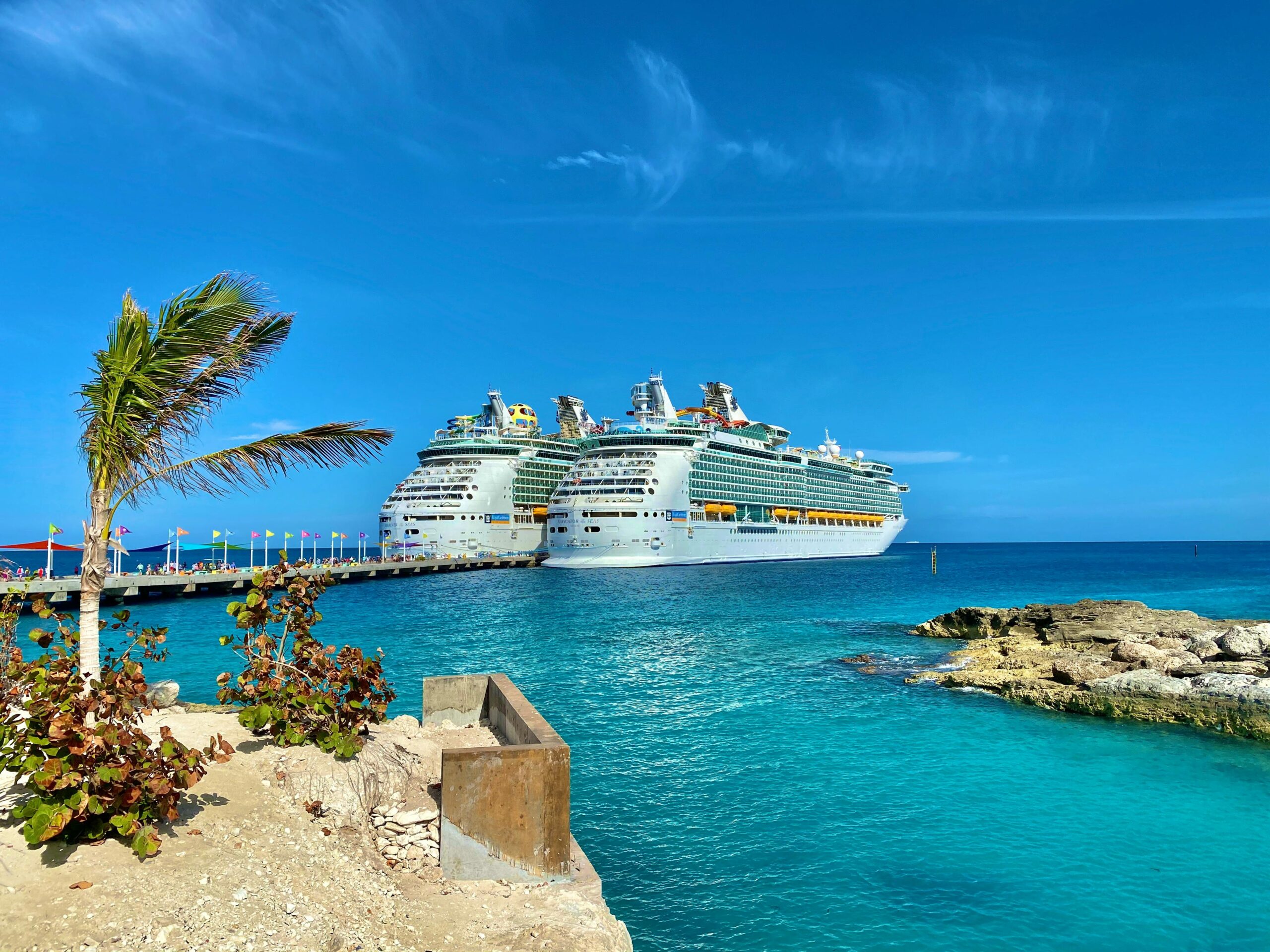 Similar big cruise ships sailing on rippled sea surrounded by small dry exotic islands and boardwalk under colorful blue sky in daylight in harbor